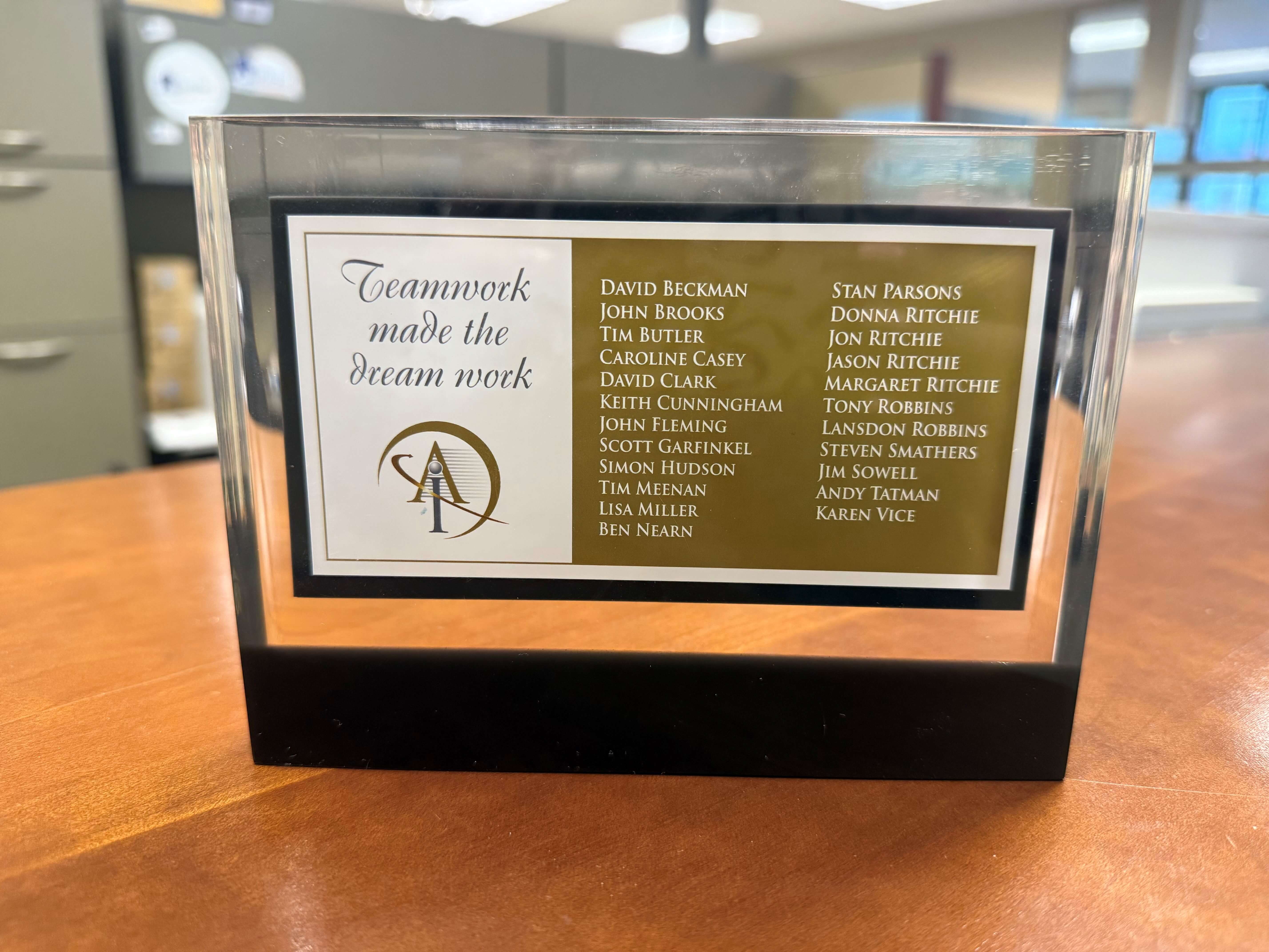 Glass plaque celebrating American Integrity's foundation in 2007 with the "Teamwork made the dream work" slogan, listing the initial team who made the dream come true