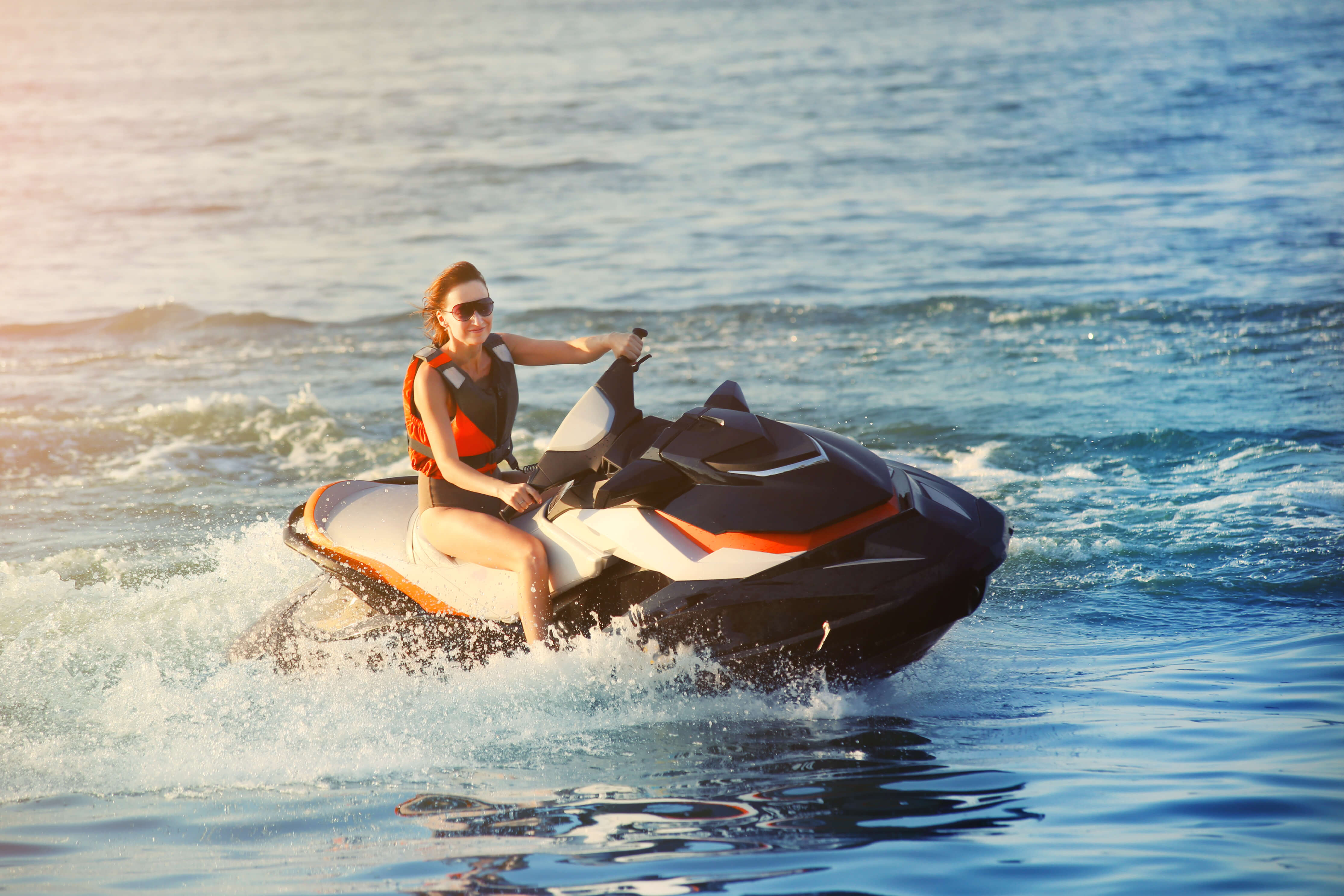 Woman in life jacket riding a jet ski in the ocean, representing the need for protection for personal watercraft