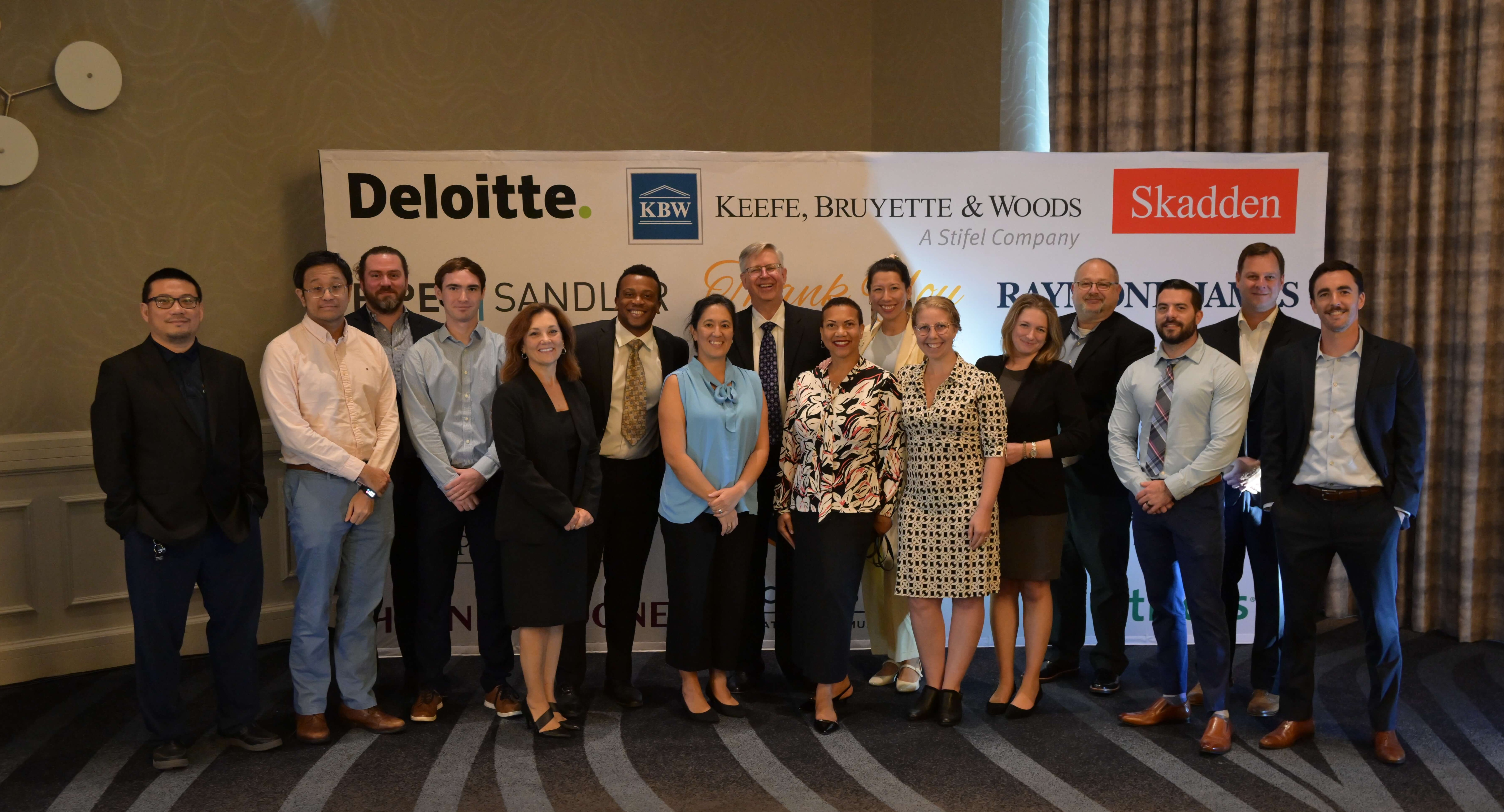Our Product Team poses for a group photo at a Town Hall event. They are posing in front of a backdrop listing our partners that supported our launch on the NYSE.